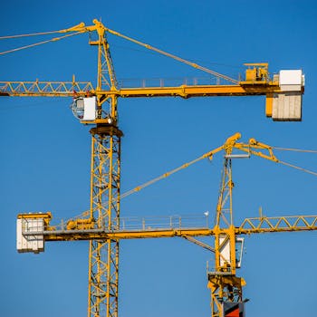 Two yellow tower cranes towering against a clear blue sky at a construction site.